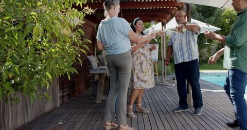 Multicultural friends toasting with wine on backyard deck by pool at summer gathering