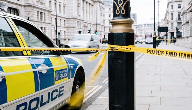 Marked police vehicle sitting behind yellow cordon on london street with blurred traffic