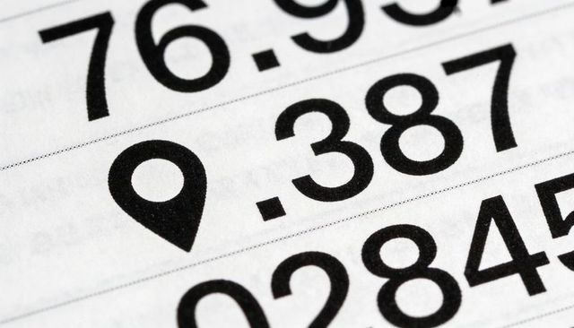Macro location-pin icon beside bold coordinates on printed list, navigation concept