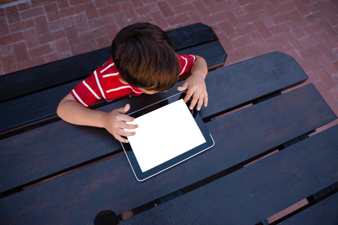 Young Boy Sitting Outdoors Using Transparent Screen Tablet at School