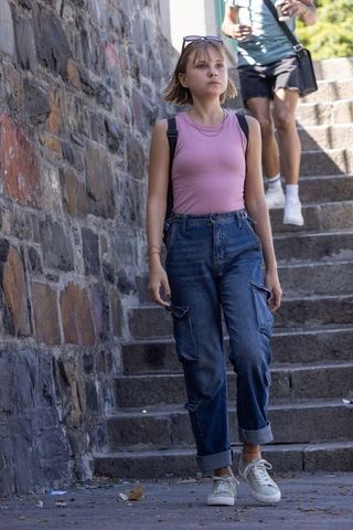 Young woman walking down stone steps wearing pink tank and cargo jeans with backpack