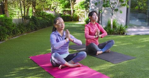 Asian mother and daughter meditating outdoors in peaceful garden setting