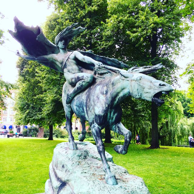 This sculpture of a mythical rider on an equestrian statue in a lush, green park is an ideal visual for highlighting public art, cultural landmarks, and detailed artworks. Its tranquil setting among the trees adds serenity, making it perfect for publications about outdoor activities, travel, art installations, and peaceful park environments.