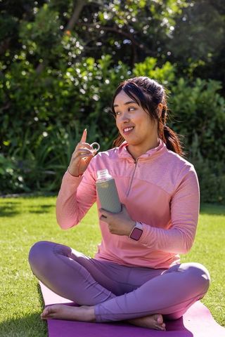African american woman practicing outdoor yoga holding reusable water bottle