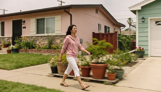 Woman walking past terracotta pots in suburban garden wearing pink hoodie and white capris