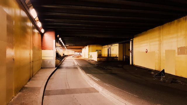 Empty tunnel glowing with artificial lighting showing a smooth paved road extending into the distance. Potential uses include urban development presentations, transportation-themed media, architectural designs, and infrastructure projects.