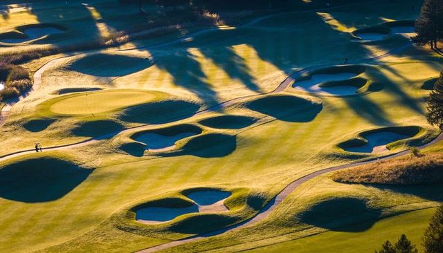 Sunlit aerial golf course with walking golfers, sculpted bunkers and winding cart paths