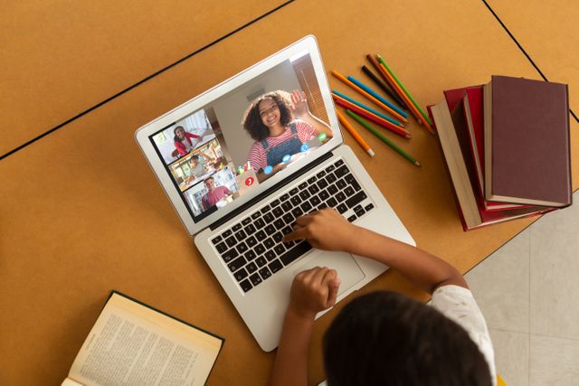 Child participating in a virtual class on a laptop, surrounded by school supplies and books. Suitable for themes of remote education, e-learning, homeschooling, technology in education, and virtual classrooms.