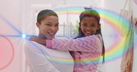 Smiling mother holding daughter in warm hug with rainbow lens flare by glass door entryway