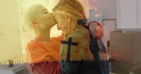 Tender forehead kiss between women hugging while packing boxes with cross double exposure