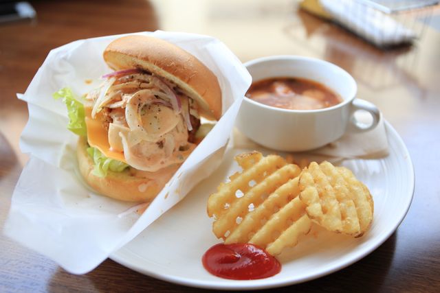 Delectable chicken sandwich layered with lettuce, cheese, and onions served with crispy waffle fries and a bowl of soup. Perfect for lunch or dinner, ideal for menus, food blogs, or advertisements promoting comfort food and dining experiences.
