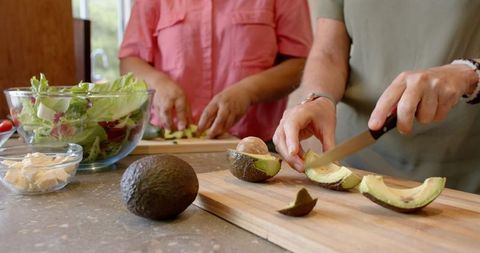 Friends preparing salad with fresh avocado at kitchen counter