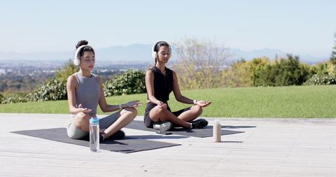 Two Women Meditating on Deck with Headphones in Scenic Landscape