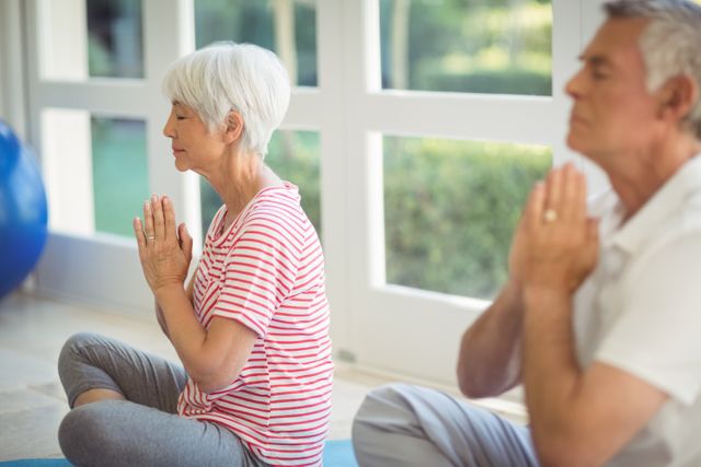 Senior couple practicing yoga at home, focusing on meditation and relaxation. Ideal for promoting healthy lifestyles, senior fitness, and mindfulness practices. Can be used in wellness blogs, fitness websites, and health-related publications.