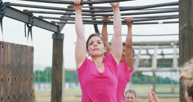 Determined caucasian women in pink t shirts hanging from monkey bars on bootcamp training course. Female fitness, challenge and healthy lifestyle.