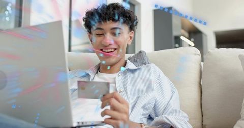 Young man using laptop and credit card on sofa with secure online shopping and fintech