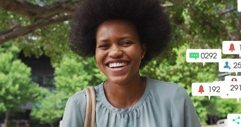 Smiling woman in urban park wearing sage green blouse with social media notification overlays