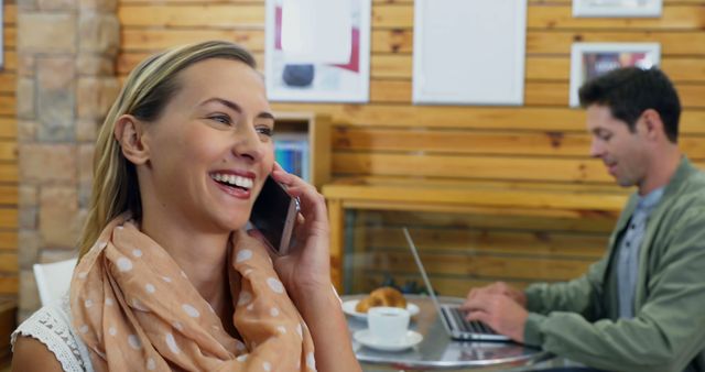 Smiling woman talking on phone in coffee shop with laptop on table - Download Free Stock Images Pikwizard.com