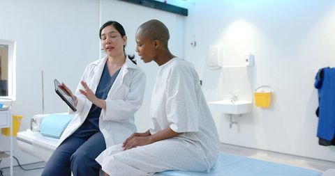 Female clinician consulting patient using tablet while seated on exam table in clinic