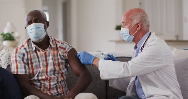 Healthcare professional administering a vaccine to a senior man sitting on a couch. Suitable for use in health-related content, websites promoting vaccination, articles about medical care, and promotional materials for healthcare services.