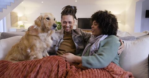 Couple cuddling on sofa with golden retriever under rust blanket, enjoying cozy moment