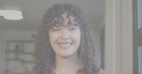 Friendly curly-haired professional smiling in office corridor with warm natural light
