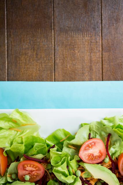 Close-up of a vibrant fresh salad with various vegetables, including lettuce and cherry tomatoes, arranged on a white plate. Ideal for use in healthy eating promotions, food blogs, restaurant menus, and diet or nutrition-related content.