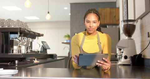 Young female barista using tablet at modern cafe counter welcoming customer service