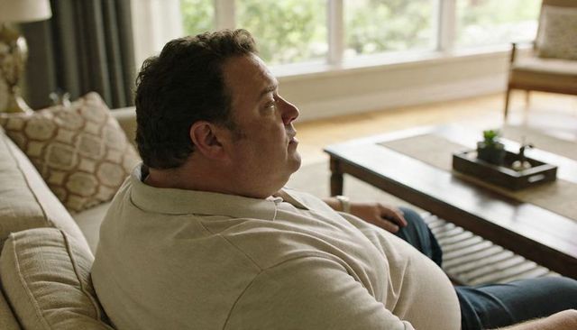 Middle-aged man relaxing on sofa wearing beige polo in sunlit cozy living room
