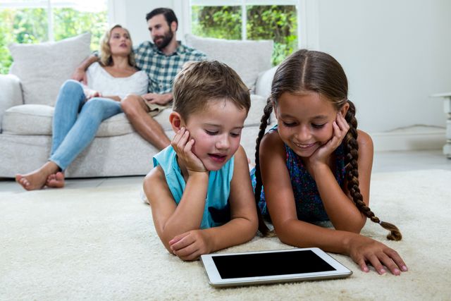 Children watching digital tablet screen while parents sitting on sofa in background