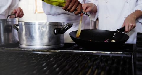 Chef Team Pouring Oil into Wok While Cooking on Commercial Stove with Stainless Pot