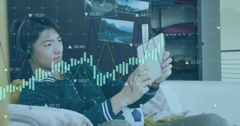Teen using tablet while reclining with headset and soccer ball, finance chart overlay