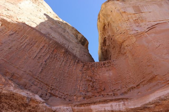 Impressive sandstone cliffs during bright sunny day with a clear blue sky. Textured rock walls create a stunning visual display perfect for nature-related content, geology studies, travel blogs, or environmental documentaries. Showcases the grandeur and beauty of natural rock formations.