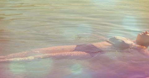 Woman floating in calm pastel lake tilting head back wearing striped swimsuit