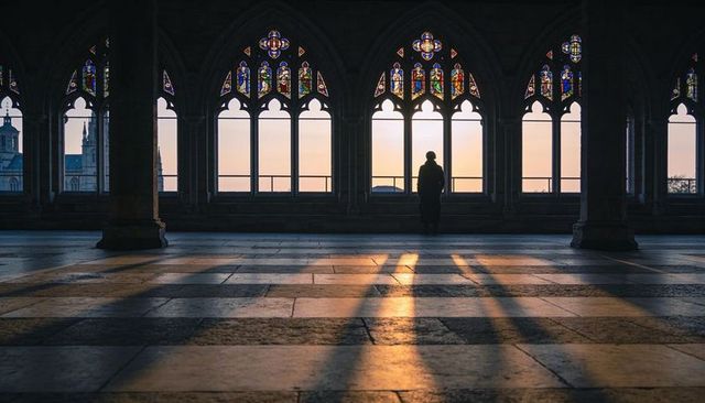 Solitary silhouette standing in gothic cathedral cloister with stained glass sunrise glow