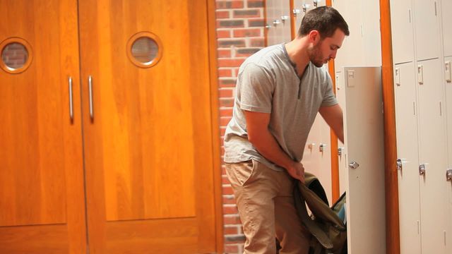 Young adult placing book into locker in school hallway. Ideal for illustrating education settings, organizational habits at school, or student-focused educational materials.