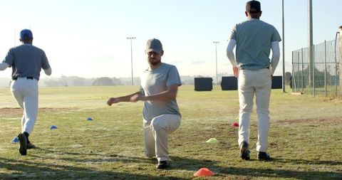 Baseball team performing warm-up drills on grass field at sunrise with colored cones
