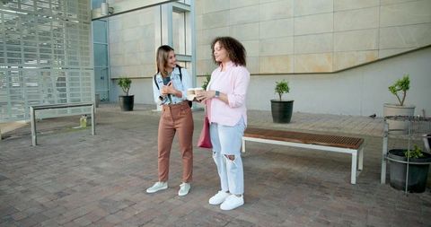 Multicultural friends walking and chatting with takeaway coffee on urban courtyard plaza