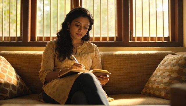 Sunlit indian woman writing in journal on living room sofa, serene home journaling