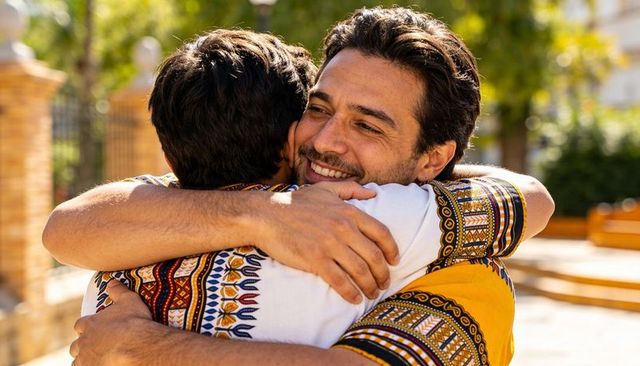 Two men reuniting with warm embrace in sunlit courtyard wearing colorful dashiki shirts