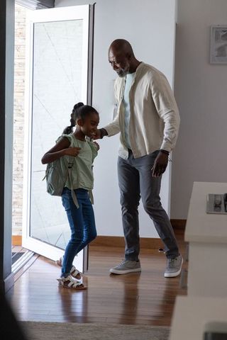 African american father adjusting daughter's backpack at front door leaving for school