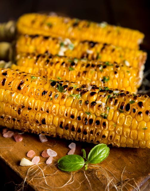 Close-up of grilled corn on the cob garnished with herb butter and pink salt. The rich golden color and grill marks represent delicious and appetizing summer barbecue food. Ideal image for food blogs, cooking websites, restaurant menus, and healthy eating promotions.