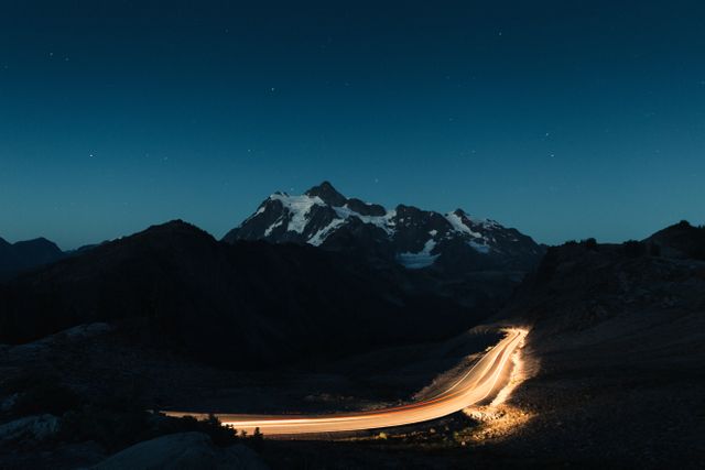 Long exposure photo capturing the lights from traffic illuminating a mountain road at twilight. Perfect for travel brochures, adventure blogs, or outdoor magazines highlighting scenic drives, night photography, or natural beauty.