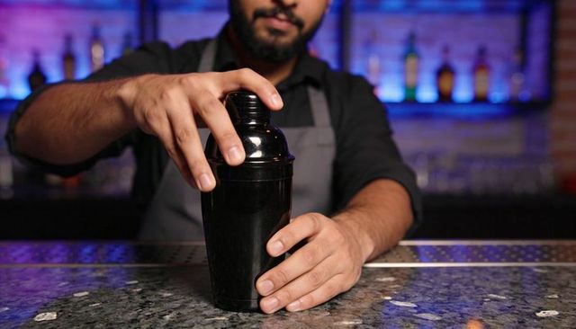 Bartender shaking cocktail shaker on backlit granite bar counter closeup for mixology