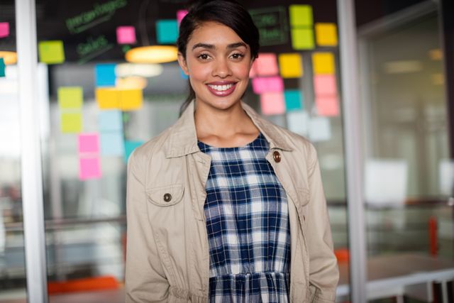 Young female executive smiling confidently in a modern office environment. Ideal for use in business-related content, corporate websites, career development materials, and professional networking profiles.