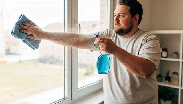 Man cleaning window with spray bottle and microfiber cloth in bright home interior