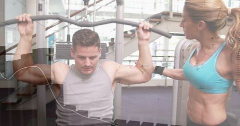 Man performing lat pulldown with female trainer guiding curved bar in modern gym