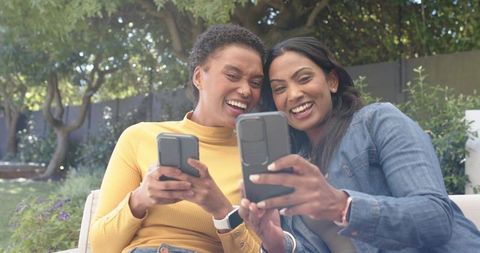 Diverse Female Friends Laughing While Sharing Smartphone Moments Outdoors