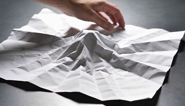 Hand adjusting crumpled white paper with dramatic creases and shadows for mockups