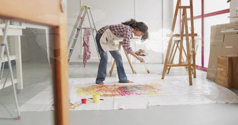 Female artist painting colorful abstract on floor canvas in bright daylight studio